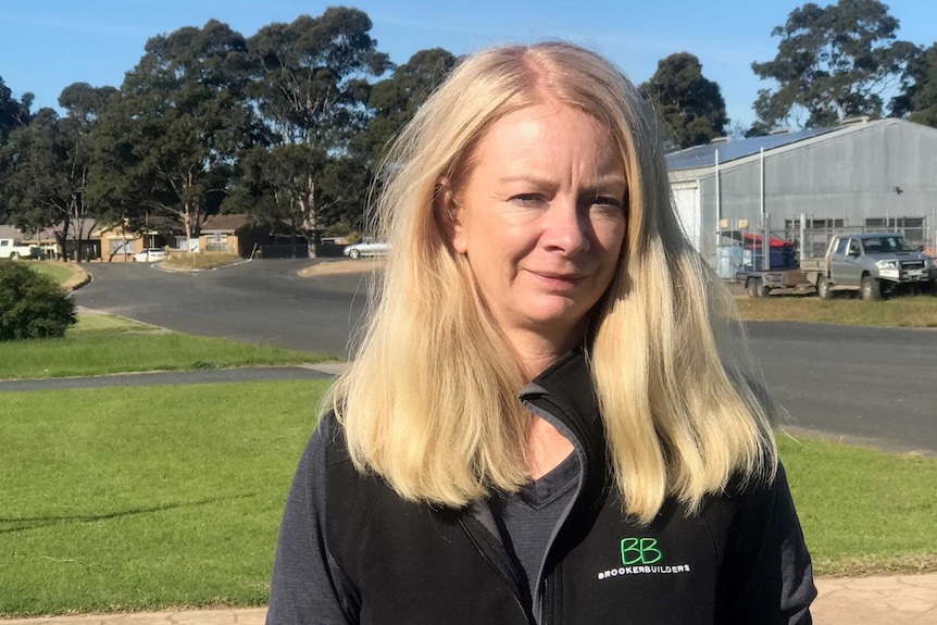 Michelle Brooker looks at the camera, behind her there is a large shed and cars.