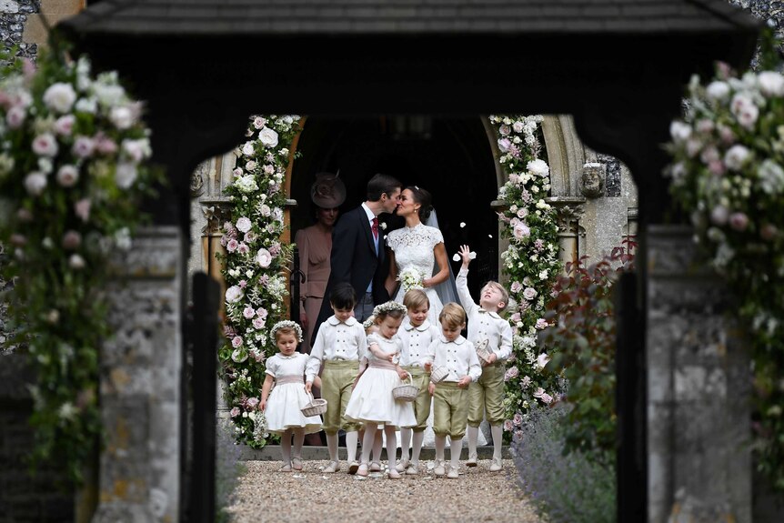 Pippa Middleton kisses her husband as their young bridal party, including Prince George and Princess Charlotte, walk ahead