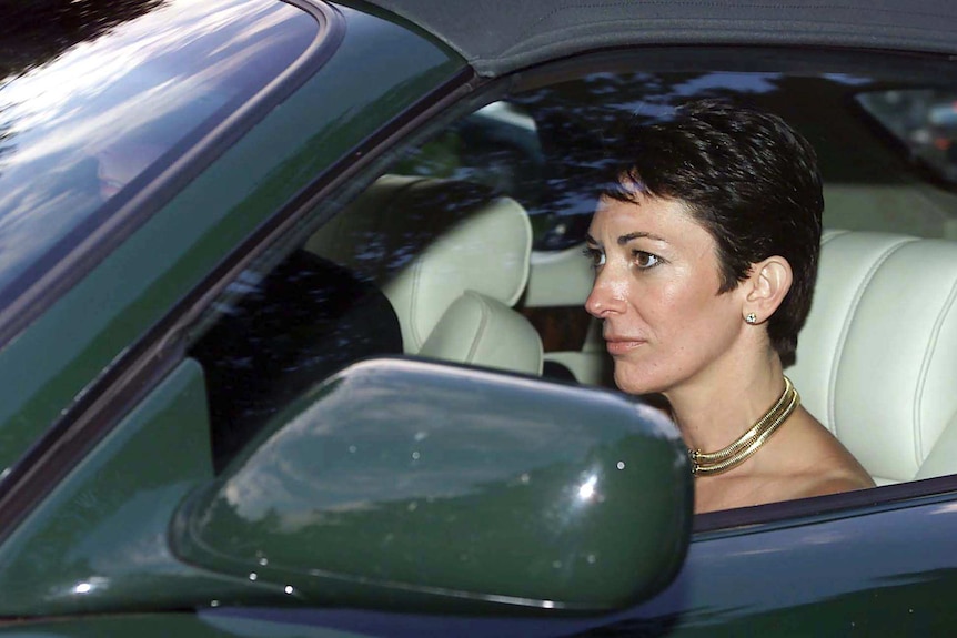 A woman with short hair drives a soft-topped sportscar , while wearing a large gold necklace.