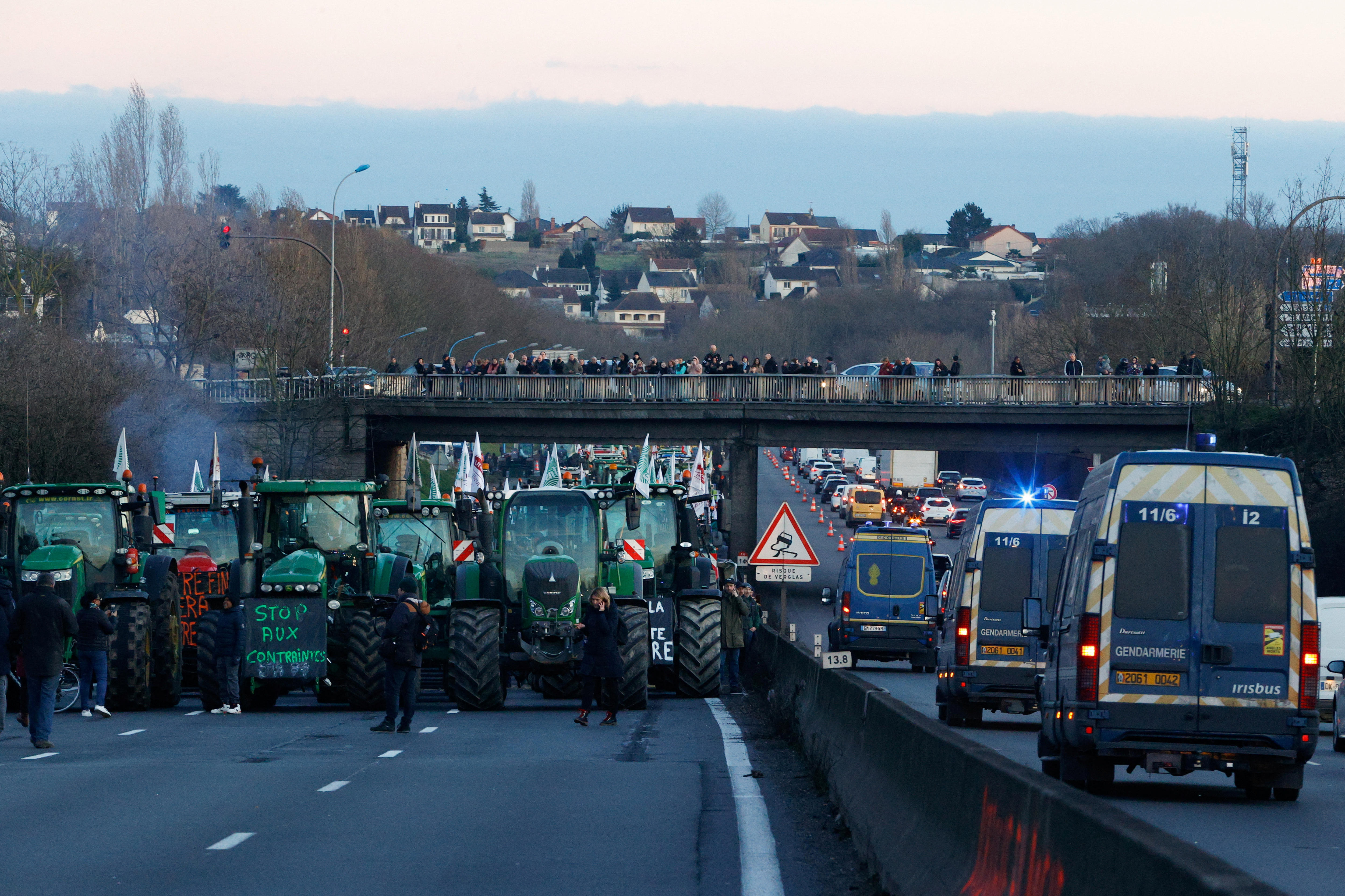 Large green tractors on the highway surrounded by people.