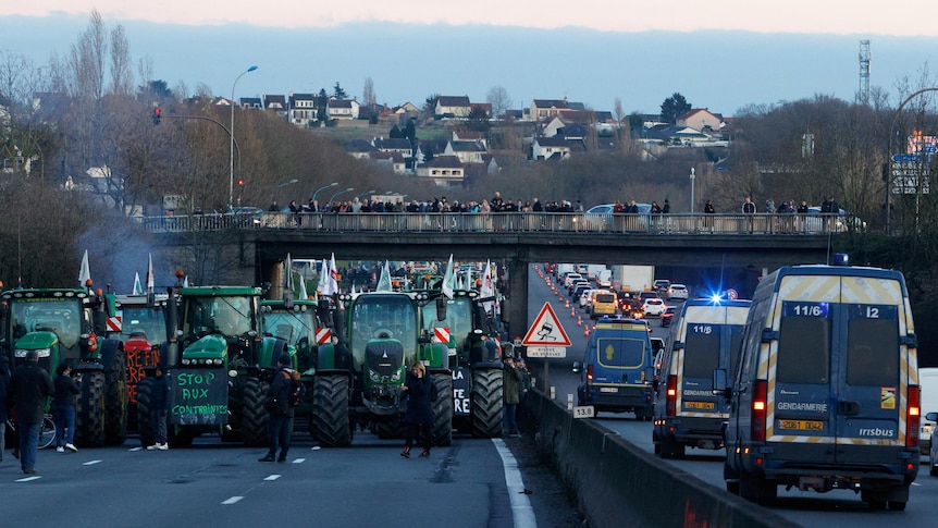 Large green tractors on the highway surrounded by people.
