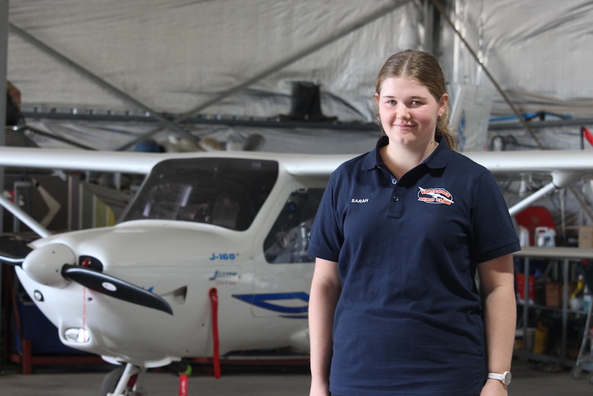 A teenage girl stands in front of a small plane. 