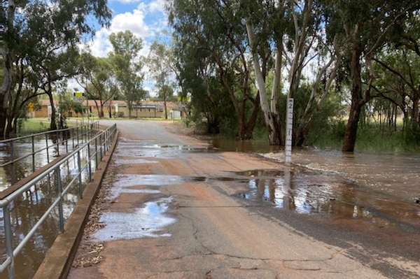 Low level creek crossing with water lapping the edge of the road.