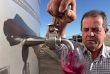 A middle-aged Italian man, Bob Franchitto, pours red wine out of a storage tank.
