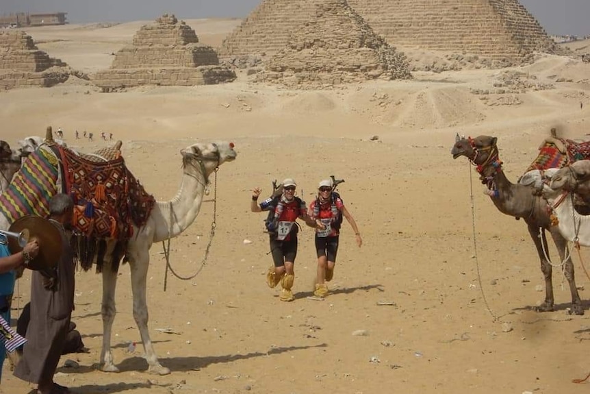 A husband and wife running in Egypt amongst pyramids and camels.