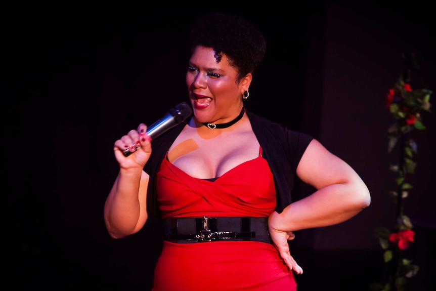 Candy Bowers wearing a red dress and performing on stage with microphone for the Australian Booty tour.