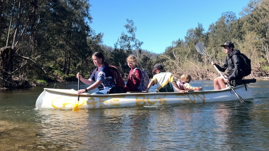 children paddle a kayak painted with the words cadgee school bus.