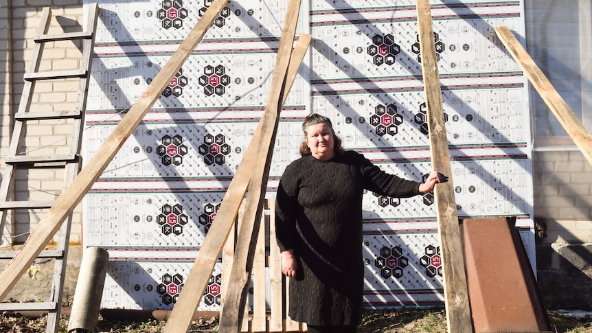 Elena Borisova wears a black coast as she holds a plank of wood supporting her house 