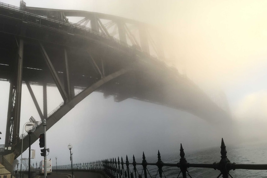 A view of the Sydney Harbour Bridge from below, shrouded in thick fog.