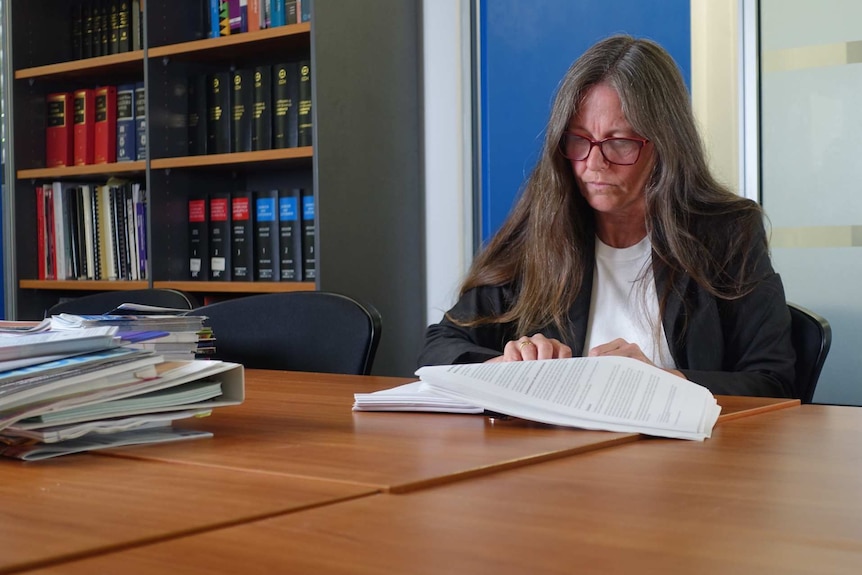 Karen Cox sit at a desk near a bookshelf and looks at documents.