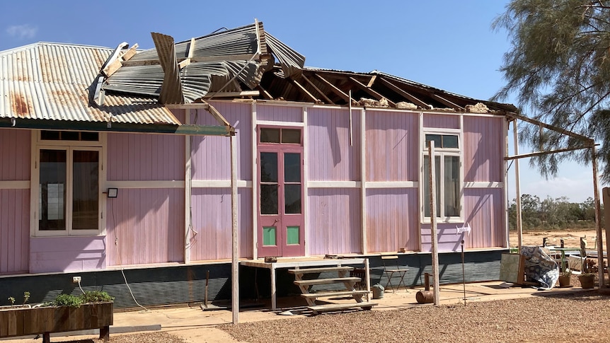 A mauve house stands with its roof half ripped off.
