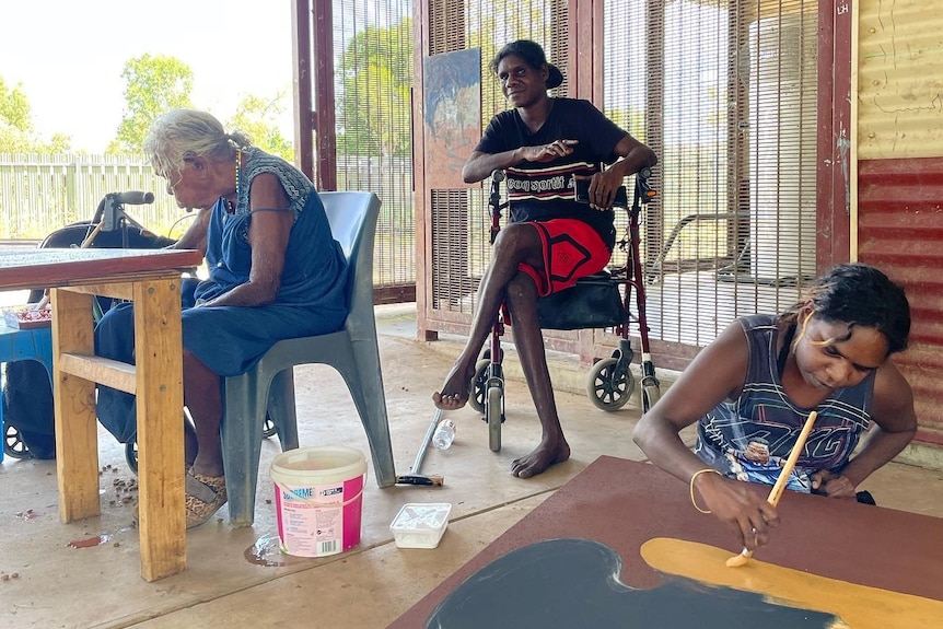 Three Indigenous women in a room, two painting, one sitting