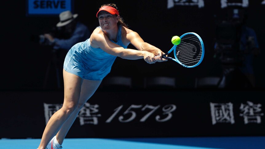 A female tennis player stretches for the ball with her teeth clenched and her racquet in both hands.