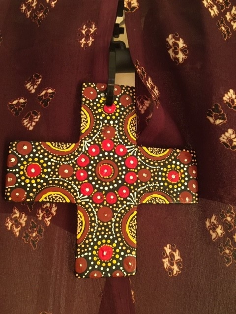 A small cross with arms of equal length, decorated with indigenous dot patterns.