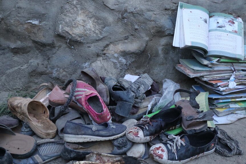 A pile of bloodied school books and shoes are piled up on the ground next to a wall.