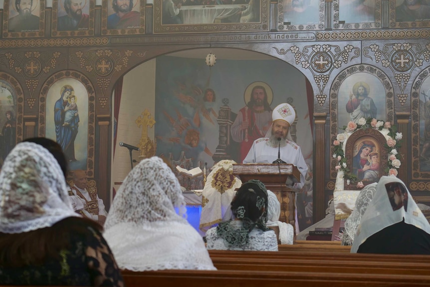Women with lace head scarfs on sitting in pews in a Coptic Orthodox church, during a service.