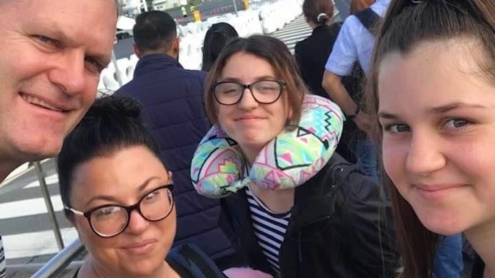 A man, woman and two younger girls pose at an airport.