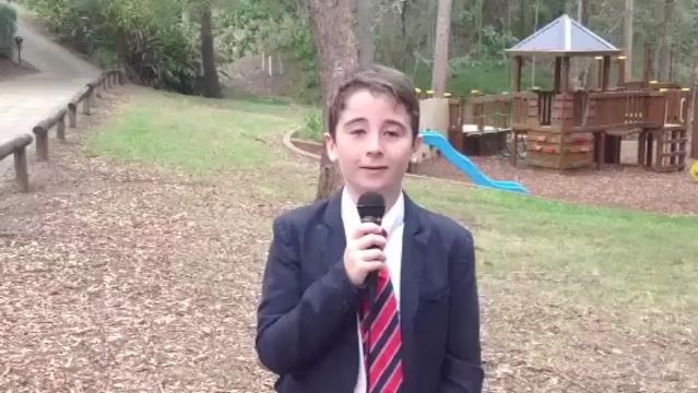 A boy dressed in a suit holds a microphone in a park