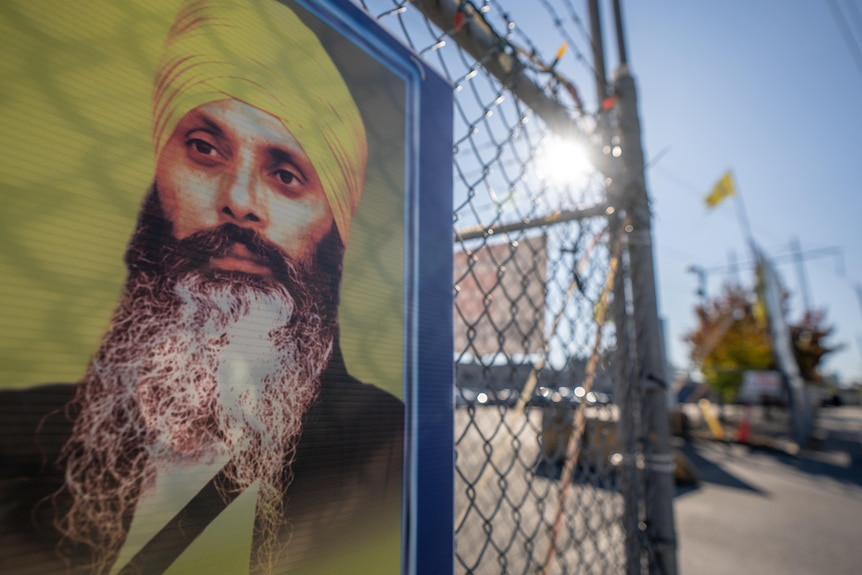 An illustration of a bearded man in a yellow turban on a yellow sign mounted on a fence.