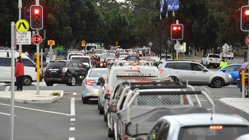 a long line of cars wait at traffic lights blocking intersection