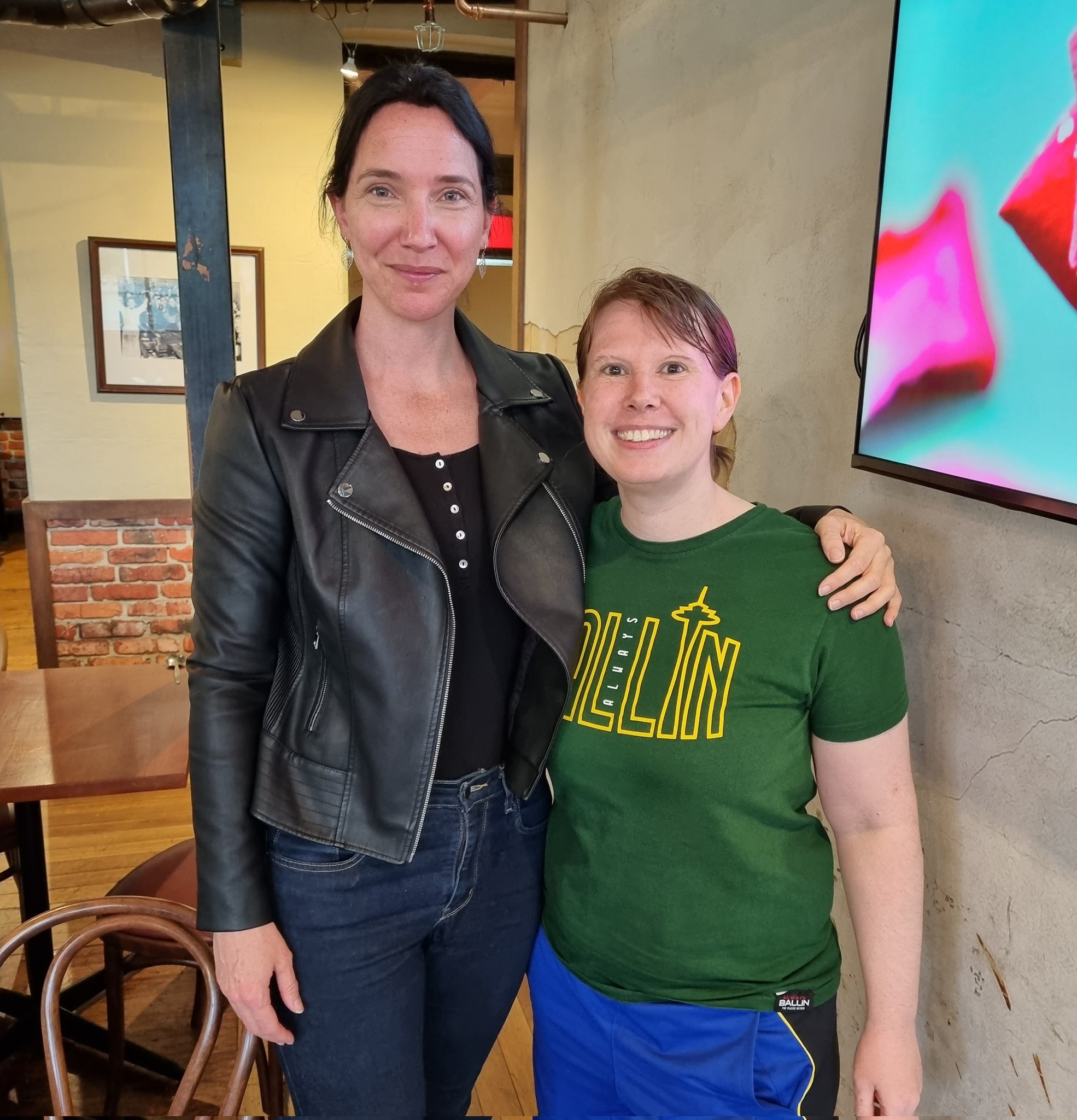 Two women stand with arms around each other, smiling at the camera.