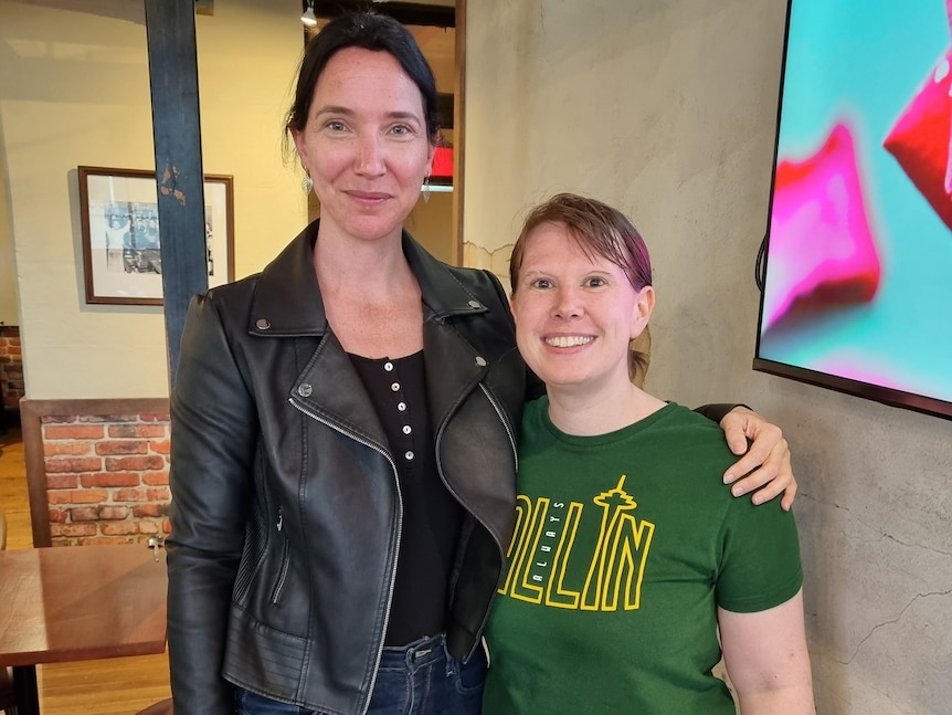 Two women stand with arms around each other, smiling at the camera.