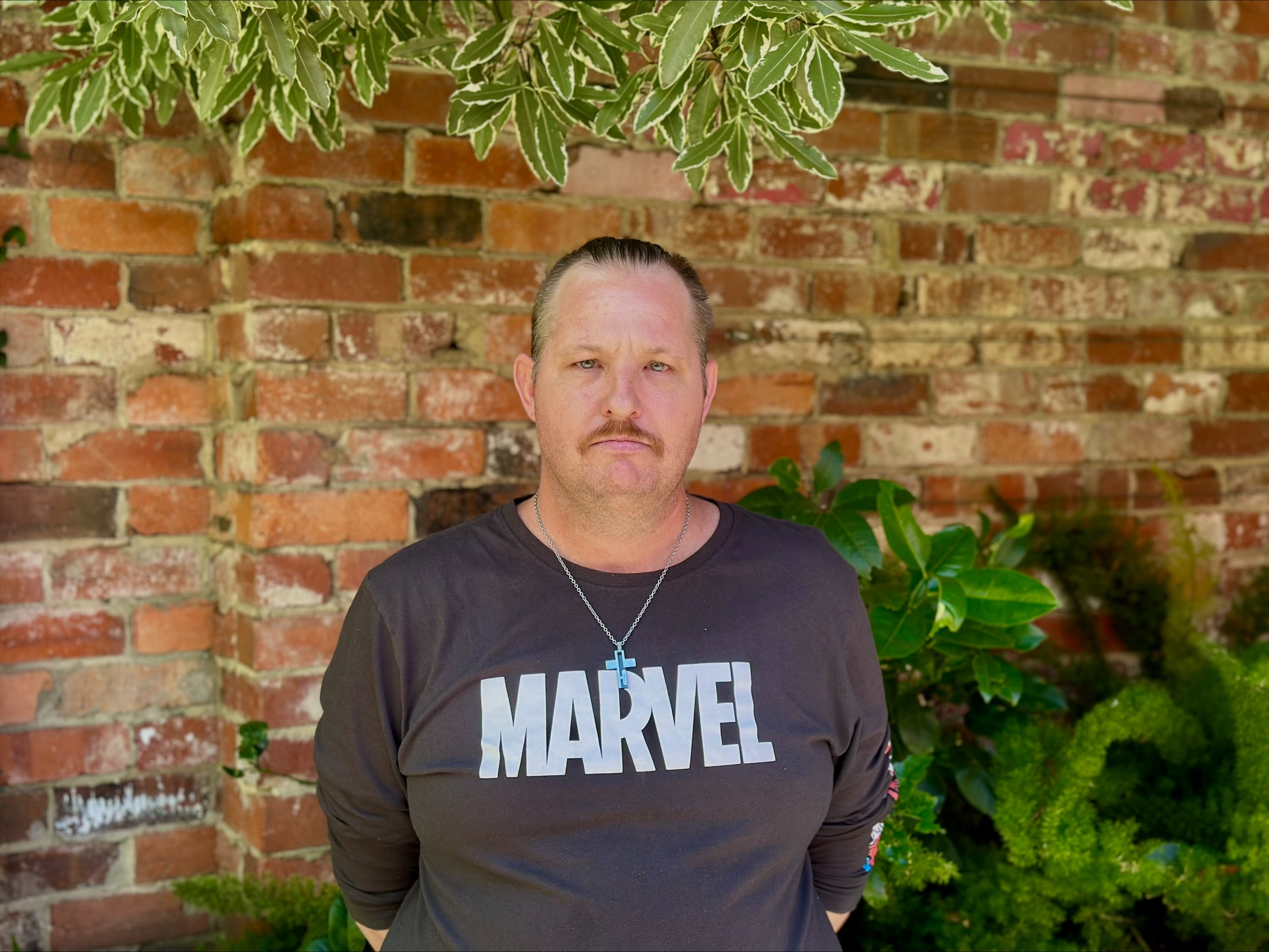 A man wearing a black t-shirt standing in front of a brick wall.