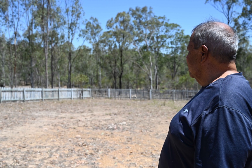 A man stands with his back to the camera observing a dry field believed to be the location of a mass burial.