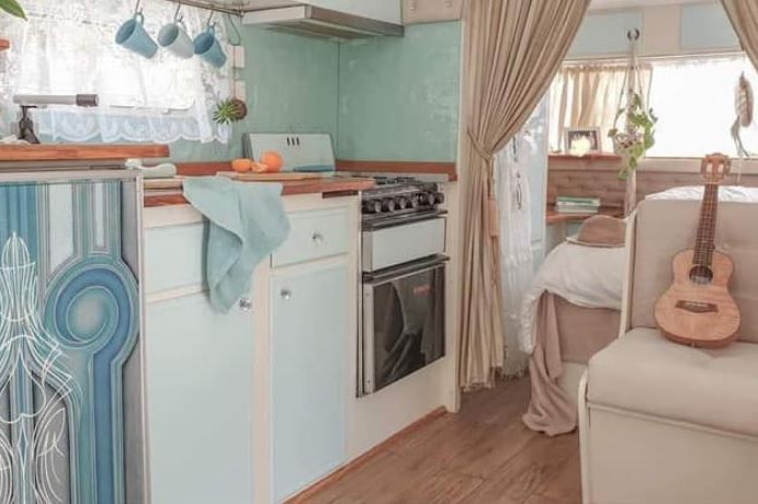 The interior of a caravan with timber kitchen benchtops and curtains separating the living area from the bedroom.