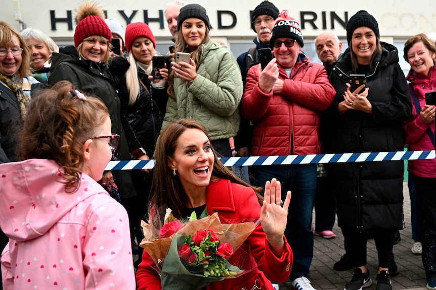 Kate collects flowers from a child and smiles and waves as she greets people in Wales.