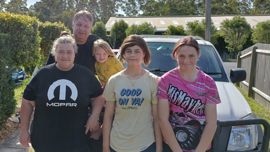 A woman and man stand in front of their 4WD car, with three children, two teenage girls and a young boy.