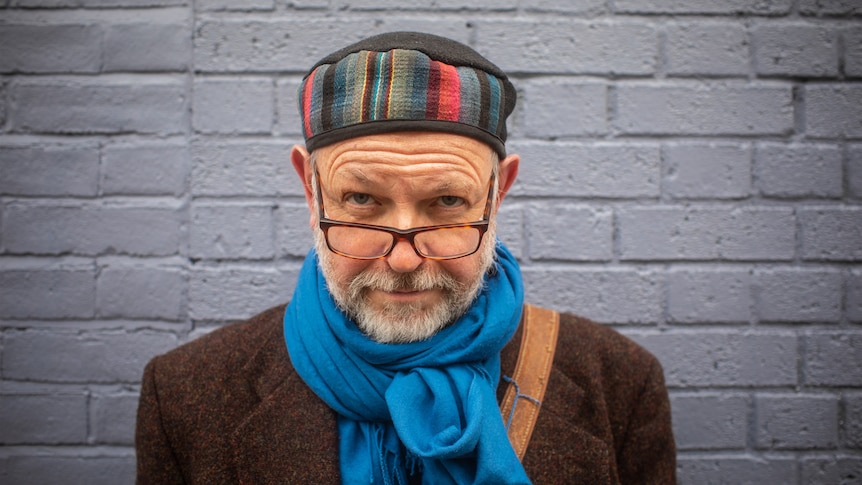 A man with a colourful hat and glasses looking at the camera