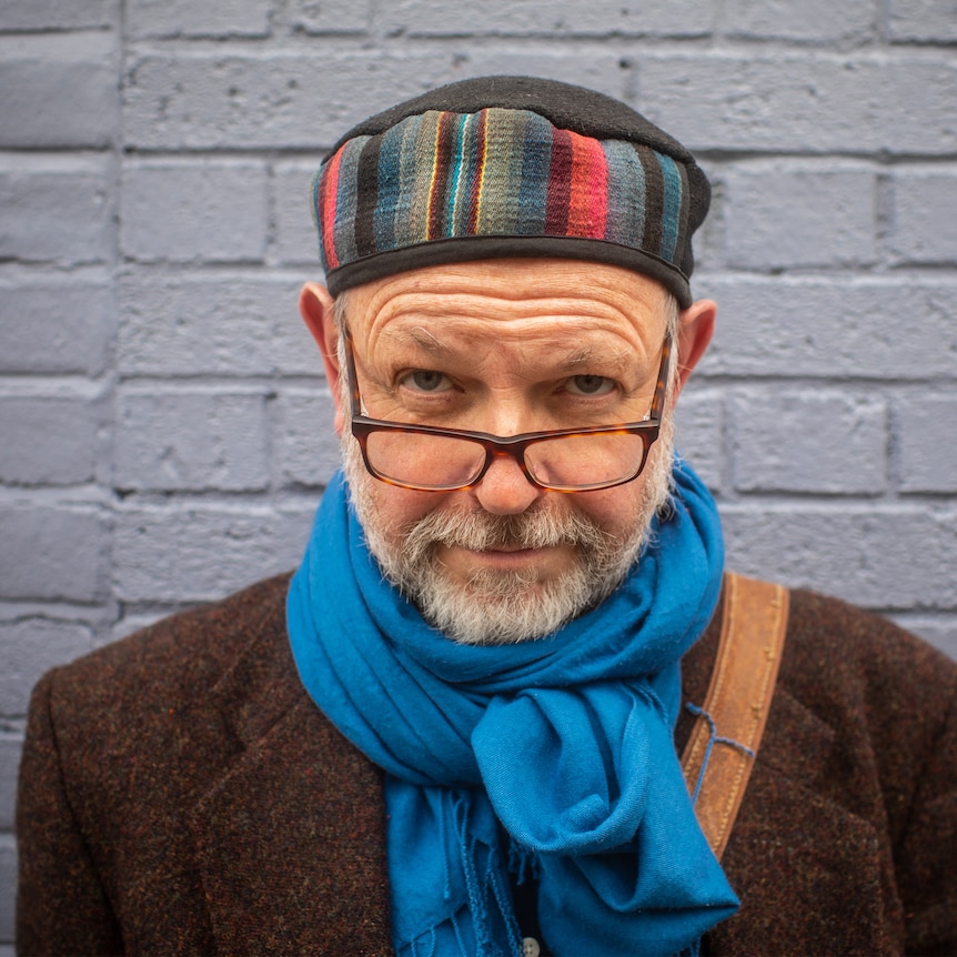A man with a colourful hat and glasses looking at the camera