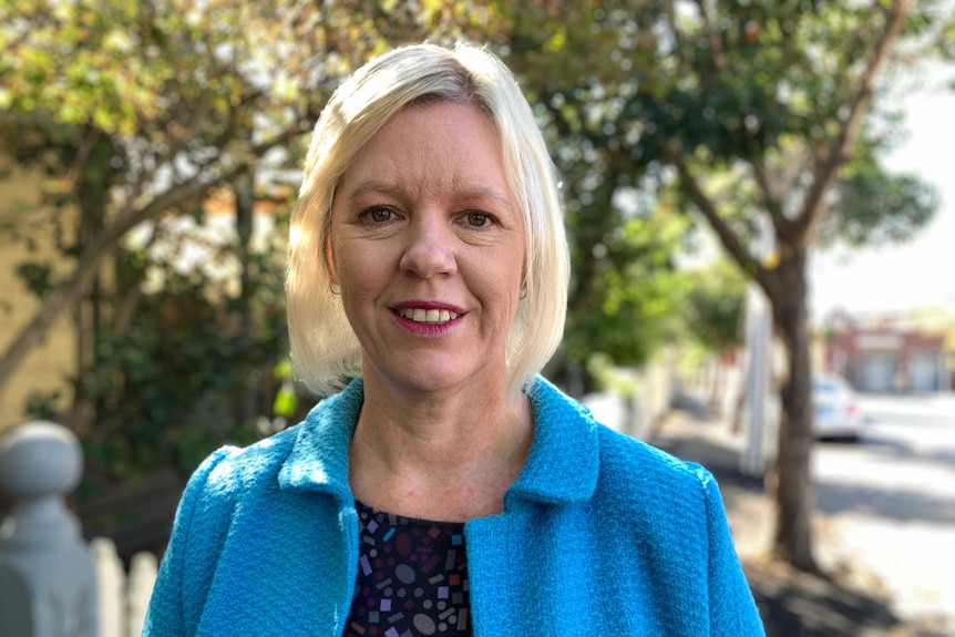 A woman wearing a blue jacket standing with some trees behind her