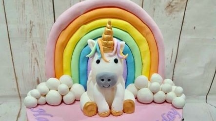Pink one tier cake with icing unicorn on top in front of an icing rainbow