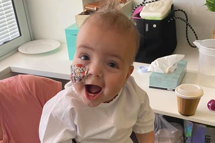 A baby named Willow looks up at the camera while standing on a man's lap