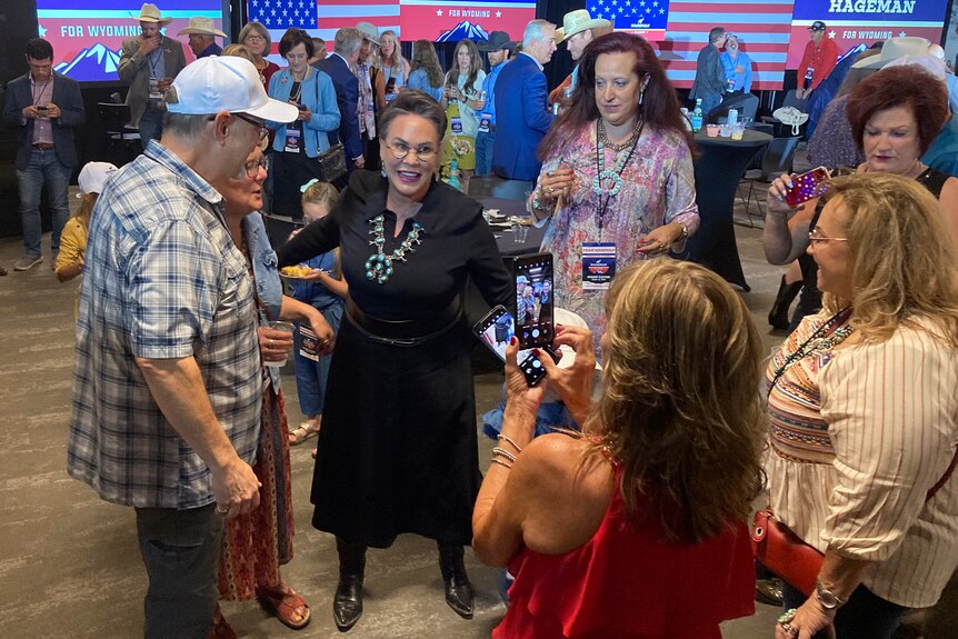 A victorious female candidate speaks to happy supporters at a busy campaing event.