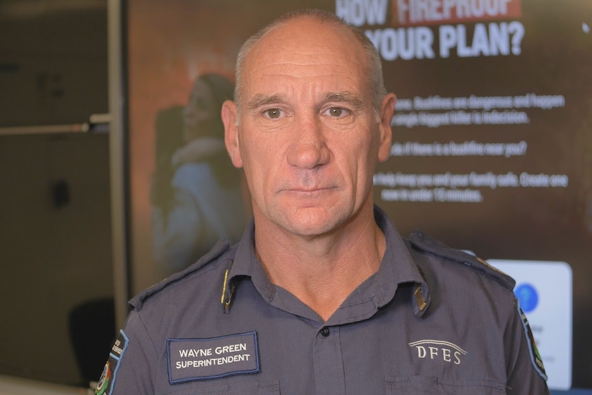 A man in a blue DFES uniform stands infront of DFES fire plan poster.