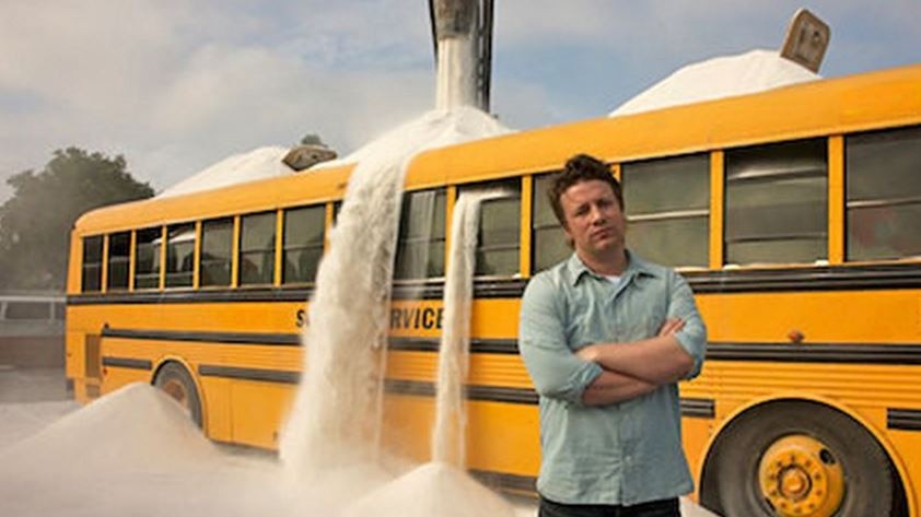 Jamie Oliver stands in front of bus overflowing with sand