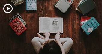 A bird's eye view of a child sitting cross-legged surrounded by books.