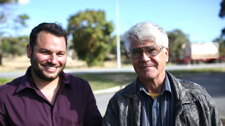 Two men in a suburban street smile for the camera.
