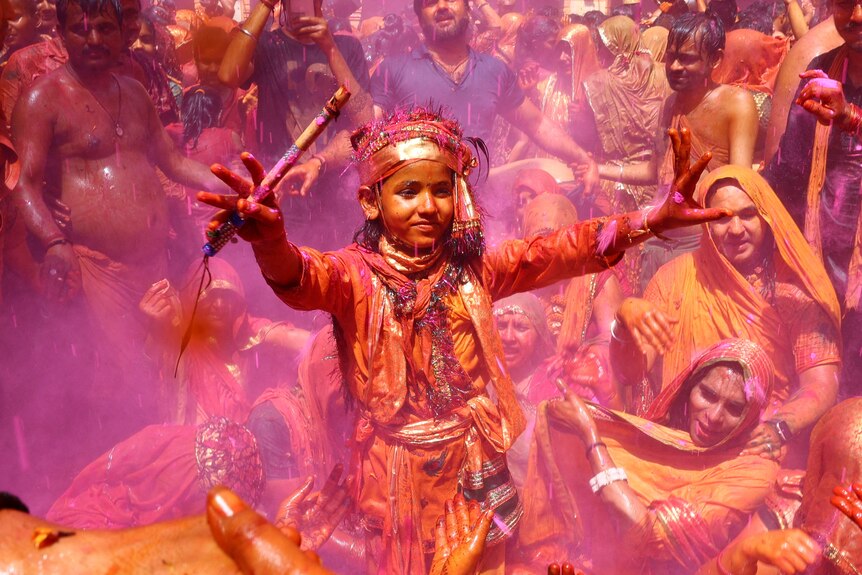 A young Hindu devotee dances in front of a crowd while covered in water and coloured powder during a ritual game at a temple.