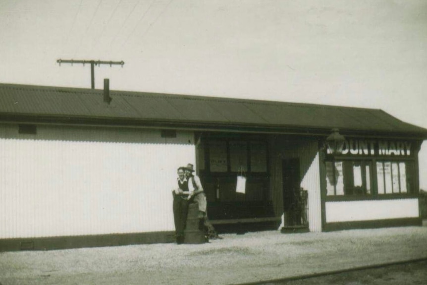Two people standing together out the front of an old railway station