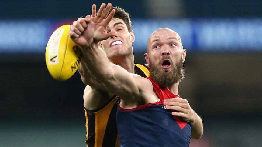 A Melbourne AFL player attempts to punch the ball while in a contest with an Hawthorn opponent.