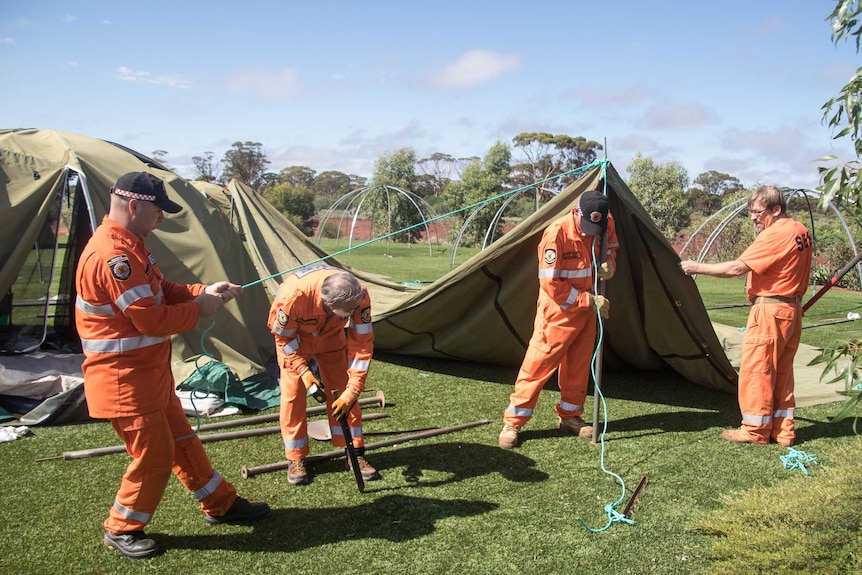 Men in orange jumpsuits put up tents