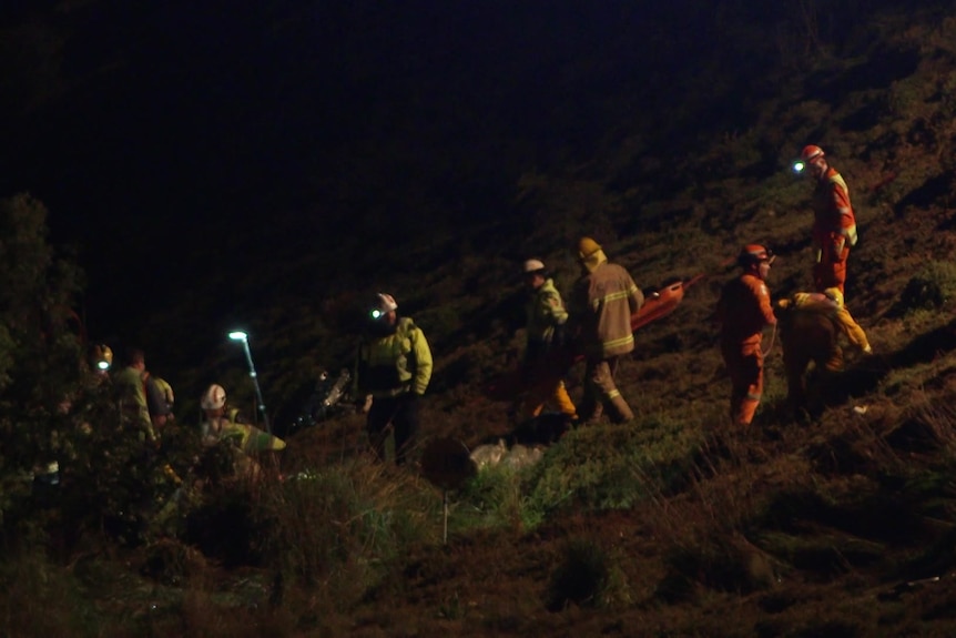 SES workers walk down an embankment at night.