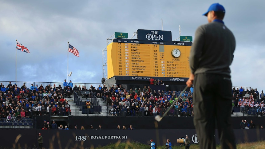 A golfer stands with his back to camera, looking at the green, with the leaderboard in front of him.