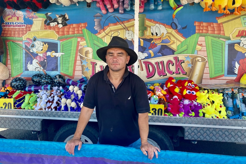 A man wearing a dark hat and shirt, standing in a sideshow alley attraction.