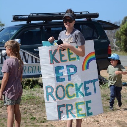 A woman standing in front of a four wheel drive holding a sign that says "Keep EP rocket free"