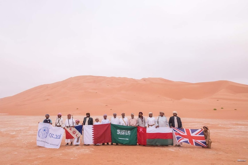 Members of the Empty Quarter expedition stand with a desert backdrop and hold flags from their country of origin